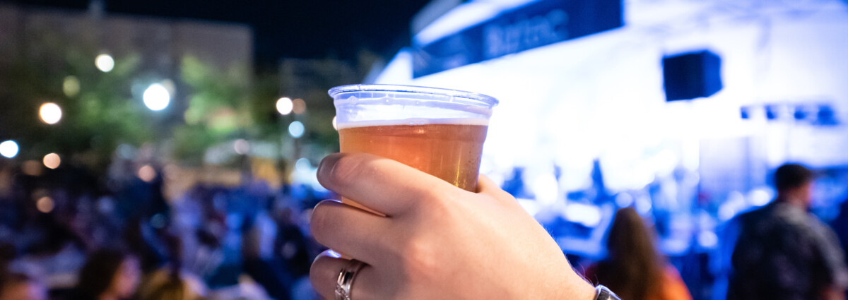 A person holding up a cup of beer at downtown brewfest.