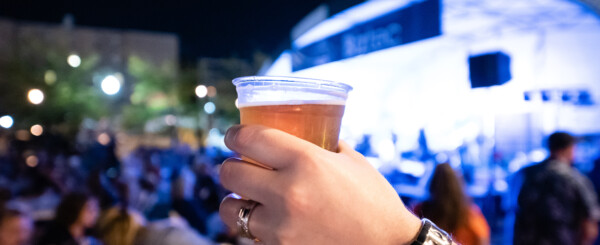 A person holding up a cup of beer at downtown brewfest.